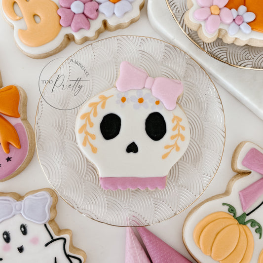 Decorative cookies shaped like a skull, ghost, and pumpkins on a white surface.