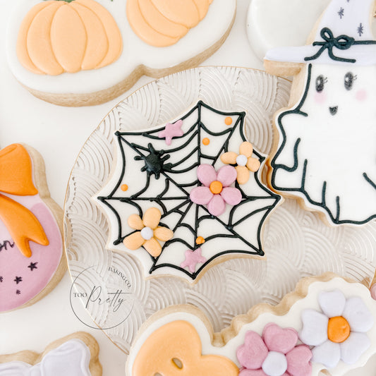 Decorative Halloween cookies with spider web, ghost, and pumpkin designs on a white background.